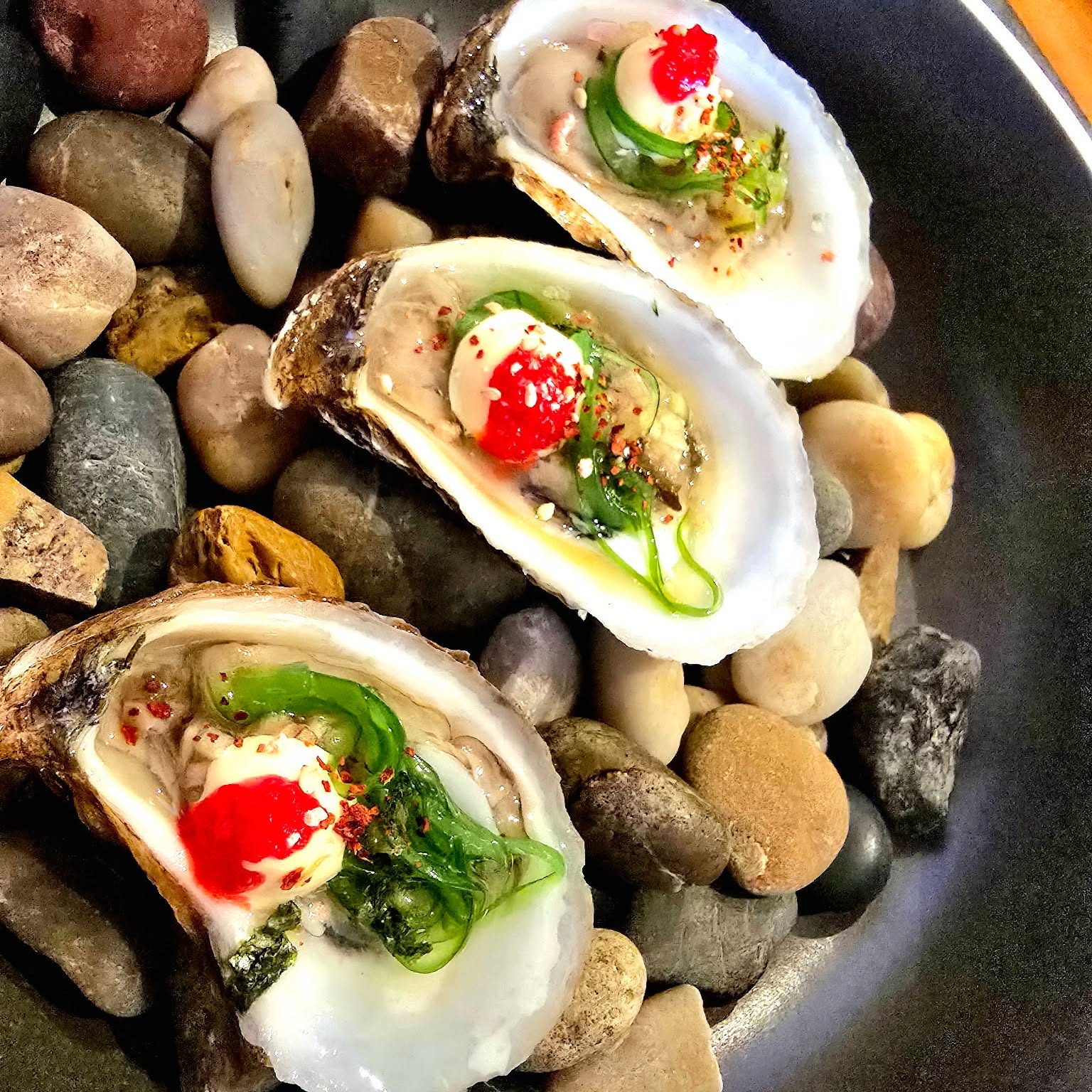 Huîtres grillées, beurre vert et piment, servies sur galets